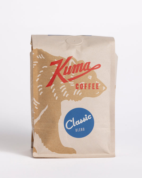 A packaged bag of Kuma Coffee's Classic blend, showing the coffee brand's logo and the word 'Classic' on a blue label, with an illustration of a bear in the background.
