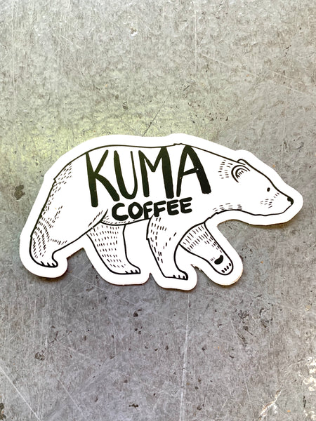 dye cut sticker of an illustration of a walking bear with the text kuma coffee written on it, concrete background 