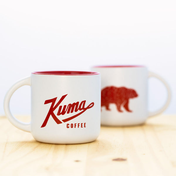 14 oz stoneware coffee mug with white exterior, Kuma Coffee logo in red on one side and bear logo in red on other side, red interior